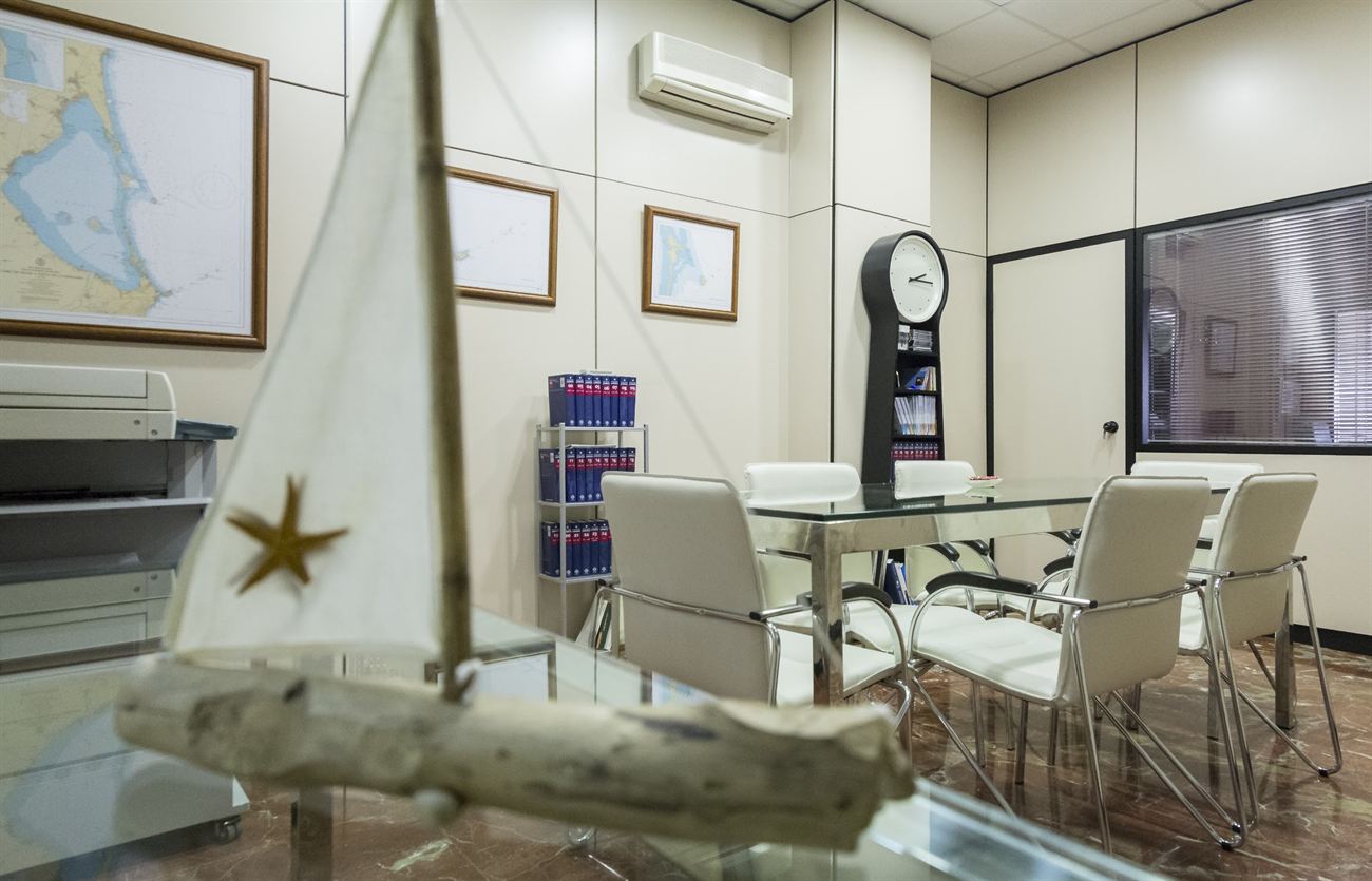 Detalle de la sala de reuniones con una maqueta de velero y las cartas náuticas de la bahía.