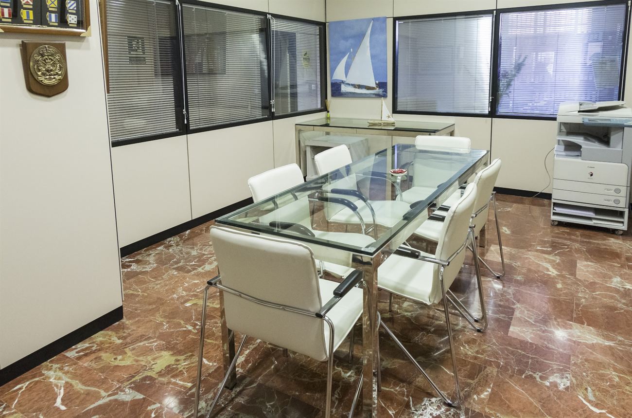 Sala de reuniones de Asesoría Cofise, con mesa de cristal y cartas náuticas en la pared.